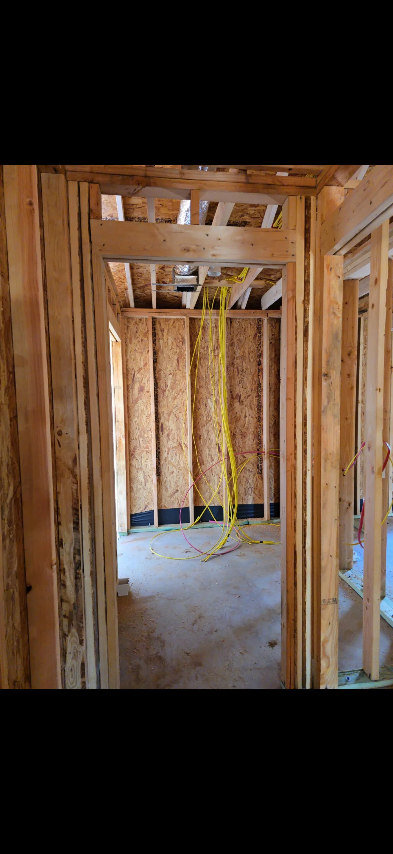 Framed residential interior with yellow electrical conduit and wiring installed in walls and ceiling