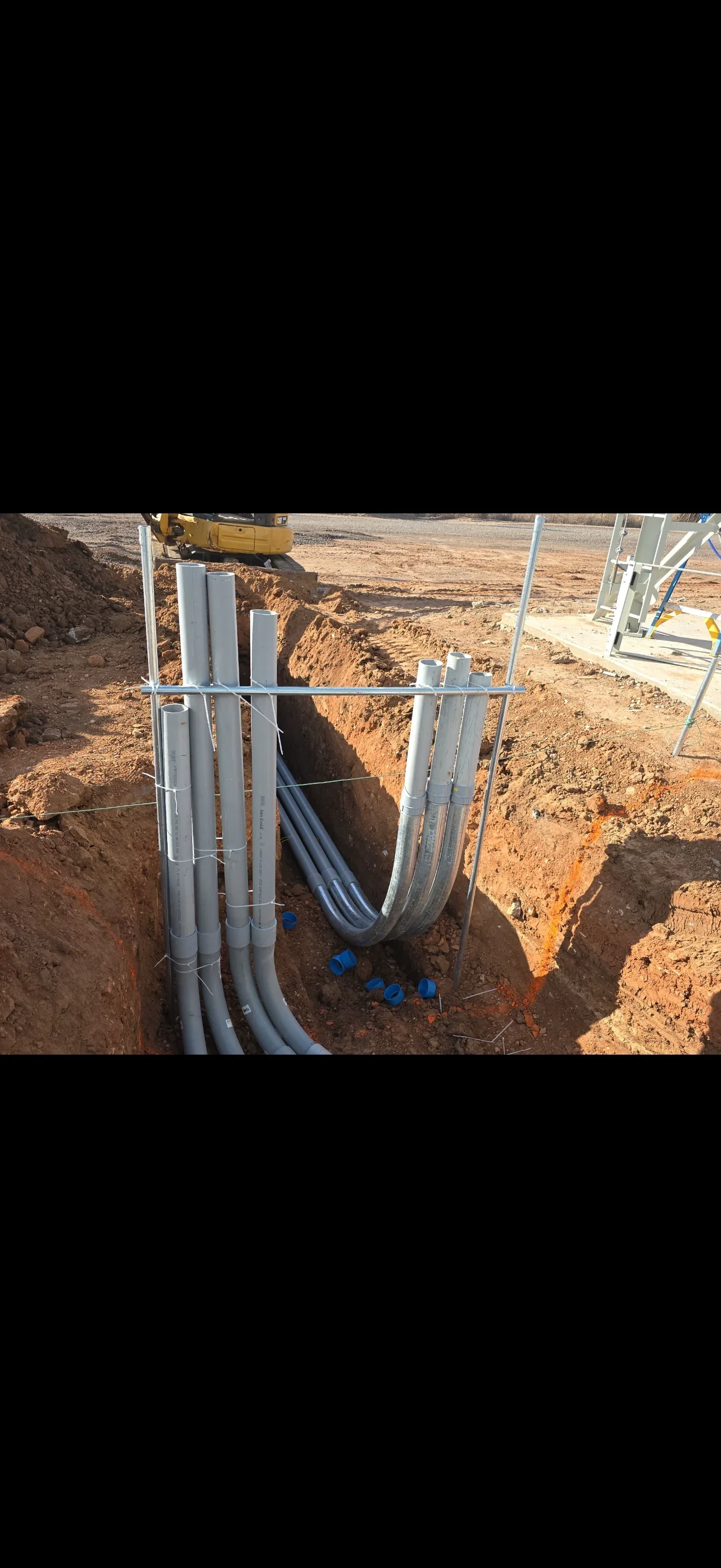 Underground PVC conduit installation with metal support frame in excavated trench