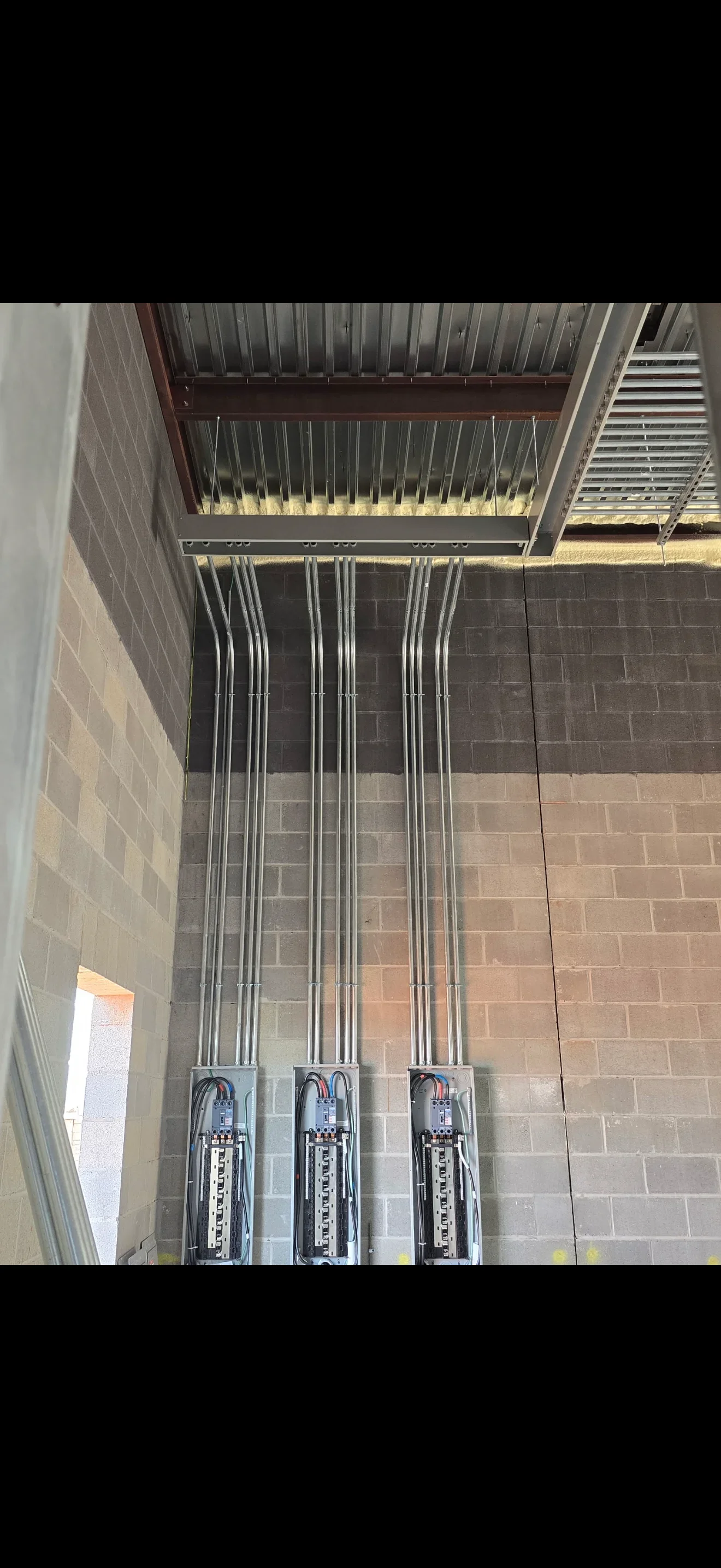 Three electrical panels mounted on brick wall with organized vertical conduit runs and circuit connections